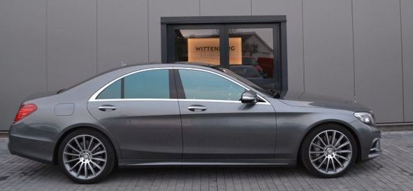 Sleek silver luxury car parked in front of a modern grey building with large windows.