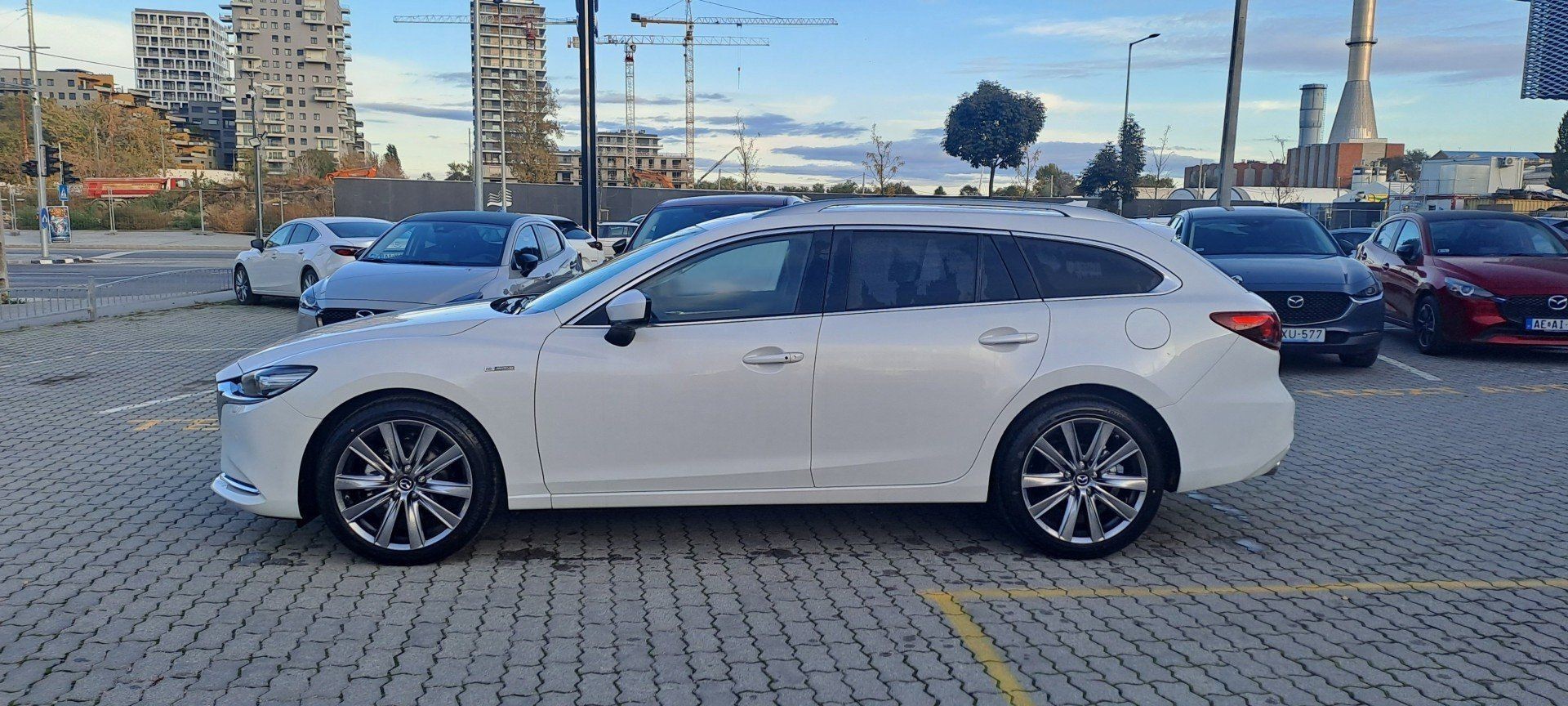 White sedan parked in a city area with buildings and cranes in the background.